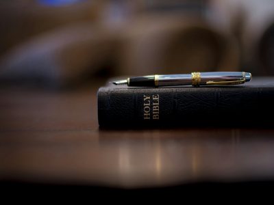 Closeup shot of the holy bible with a fountain pen on top and a blurred background